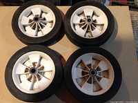 Top view showing white plastic spokes, metal centers, and black rubber tires of four wheels arranged in a square on a cardboard surface.