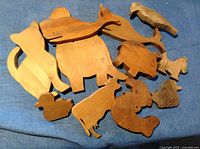 Image of twelve handmade wooden animal cutouts displayed on a blue fabric background, showing various animal shapes like cat, whale, elephant, cow, duck, dog, bird, rabbit, squirrel, mouse, dinosaur, insect.