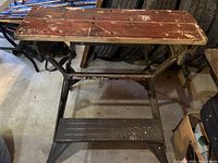 Front and top view of a Black & Decker Workmate portable workbench showing brown wooden top with visible wear and black metal legs.