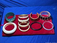 Mixed bracelets displayed on red velvet cloth, showing a variety of plastic and carved wood bangles with intricate and simple designs.
