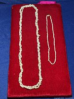 Two rice pearl necklaces with 14k yellow gold clasps laid on a red velvet surface.