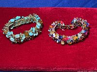 Two beaded bracelets displayed on a red surface; one turquoise beaded with amber stones, the other multicolored glass bead bracelet.