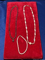 Photo showing all three items: black pearl necklace with amethyst pendant, white pearl necklace, white pearl bracelet, displayed on red velvet