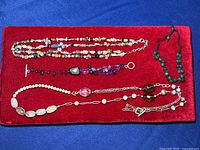 Four jewelry items arranged on red velvet including two necklaces and two bracelets