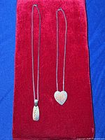 Two stainless steel chain necklaces on red velvet background; one with a rectangular copper pendant, the other with a heart-shaped sterling silver and copper pendant