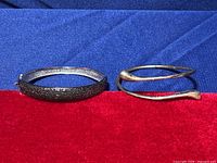 Two bracelets placed side by side on a red velvet surface, one bypass style and one with black diamond chips covering outer surface.