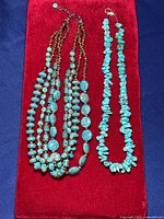 Two necklaces placed on a red velvet background: one multi-strand with polished turquoise and brown beads, the other single strand with irregular turquoise chip beads.