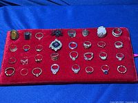 Lot of 32 mixed metal rings displayed on red velvet fabric against blue background