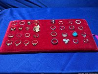Overview of 32 mixed metal rings on a red velvet tray.
