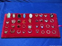 Full display of 36 silver and gold rings on a red velvet pad, showing their varied designs and stones.