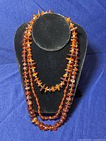 Front view of the 3 amber necklaces displayed on black velvet neck stand showing different bead shapes and colors.