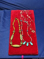 Full view of all three beaded necklaces on a red velvet surface against navy background