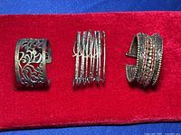 Front view of three brass tone and beaded cuff bracelets on red fabric