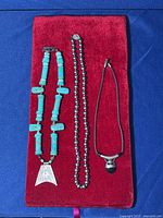 Three necklaces laid out on red velvet fabric: Howlite turquoise necklace with silver-tone triangular pendant on left, faux black pearl bead necklace in middle, silver-tone necklace with black faux onyx pendant on right.