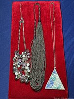Full view of all three necklaces on red background showing different styles and designs