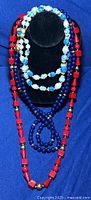 Full view of three plastic bead necklaces on display with different bead colors and goat/ram clasp visible on white and blue necklace.