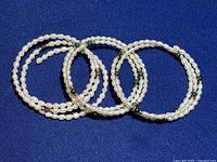 Three white rice pearl bracelets with green and silver bead accents on a blue background.