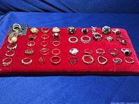 Full view of 40 rings arranged neatly on red display pad showing variety in metal tones and styles.