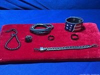 Full lot of four bracelets and three rings arranged on red velvet cloth, showing variety of styles and materials.