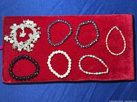 Seven stretch bracelets including a silver-tone charm bracelet, multiple blue faceted bead bracelets, a pink bead bracelet, a black bead bracelet, and a white bead bracelet arranged on a red background.
