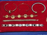 Eight mixed-metal bracelets displayed on red velvet background, showing variety of styles and materials.
