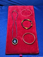 Five jewelry pieces on a red velvet background including a necklace with a large faceted Smokey Quartz pendant and four bracelets of varied style and color.