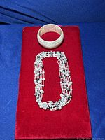 Photo showing the pearl necklace and mother of pearl bangle bracelet displayed on a red velvet surface.