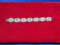 Full view of the vintage 925 sterling silver bracelet with seven flower-shaped links featuring amethyst stones laid out on red fabric.