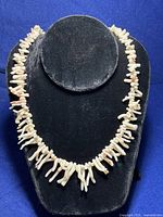 Close-up photo showcasing the ivory white coral branches and rose coral accents on black necklace display bust.