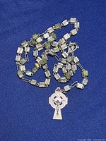 Close-up photo of one rosary showing square green Connemara stone beads linked with metal and Celtic cross pendant on a blue fabric background.