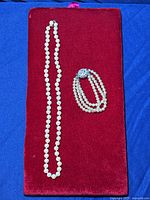 Full view of the faux glass pearl necklace and 7 strand bracelet on a red velvet background.
