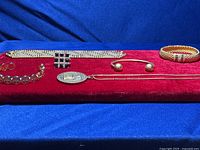 Lot of 6 pieces of gold tone jewelry on red velvet display including 4 bracelets, 1 ring, and 1 coin pendant with chain.