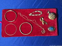 Full lot of gold tone jewelry on red velvet pad against blue background showing bracelets, necklace, two brooches, and pocket watch.