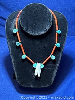 Front view of Indigenous American necklace with red coral beads, turquoise stones, and mother of pearl pendant displayed on black stand.