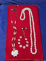 Full lot displayed on red fabric background with all three jade jewelry pieces: two necklaces and one bracelet.