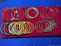Top view of assorted bangle bracelets arranged on a red velvet surface, showing a variety of metal and plastic bangles.