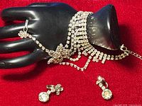 Bracelet displayed on a black mannequin hand with matching clip-on earrings on a red background.