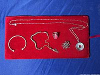 Full lot with two bracelets, one ring, one brooch, silver chain, and round mother-of-pearl pendant on red velvet background.