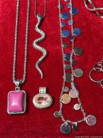 Close-up view of three necklaces showing snake-shaped chain, pink stone pendant, and coin charm chain with oval gemstone pendant nearby.