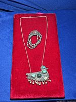 Top view of silver plated necklace with bird pendant and multi-strand silver plated bracelet on red background
