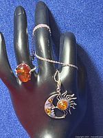 Sterling silver amber ring worn on a display hand, necklace with sun and moon amber pendant draped on fingers.