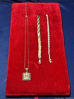 Lot of one sterling silver necklace with square pendant and two sterling silver bracelets displayed on red velvet fabric.