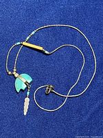 Sterling silver chain necklace with turquoise bear pendant and feather charm, laid out on blue fabric background.