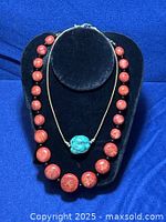 Photo showing coral bead necklace and turquoise bead necklace displayed on a black stand with blue background.