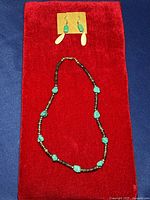 Full view of the turquoise necklace with wooden beads and pair of earrings placed on a red fabric background.
