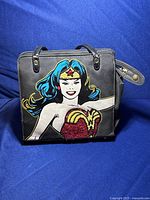 Front view showing colorful Wonder Woman comic design with red glitter emblem on black purse.