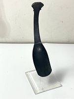 Front angle view of the carved wooden ceremonial rice spoon on a clear stand.