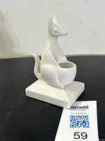 Front angled view of white porcelain kangaroo match strike on black surface with auction tag visible.