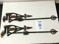 Top view of pair of ornate cast iron arrow-shaped swing arm curtain rods with brackets, showing red and green paint highlights and arrow detail