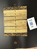 Palm leaf manuscript laid flat showing six broad horizontal strips with faint etched narrative scenes, bordered by carved floral wooden covers at top and bottom. Original binding with string and Chinese coin present.